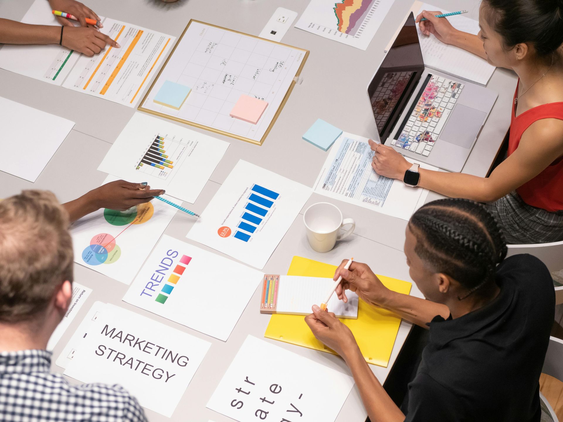 A diverse group of colleagues collaborate around a table, reviewing marketing strategy documents and charts together.