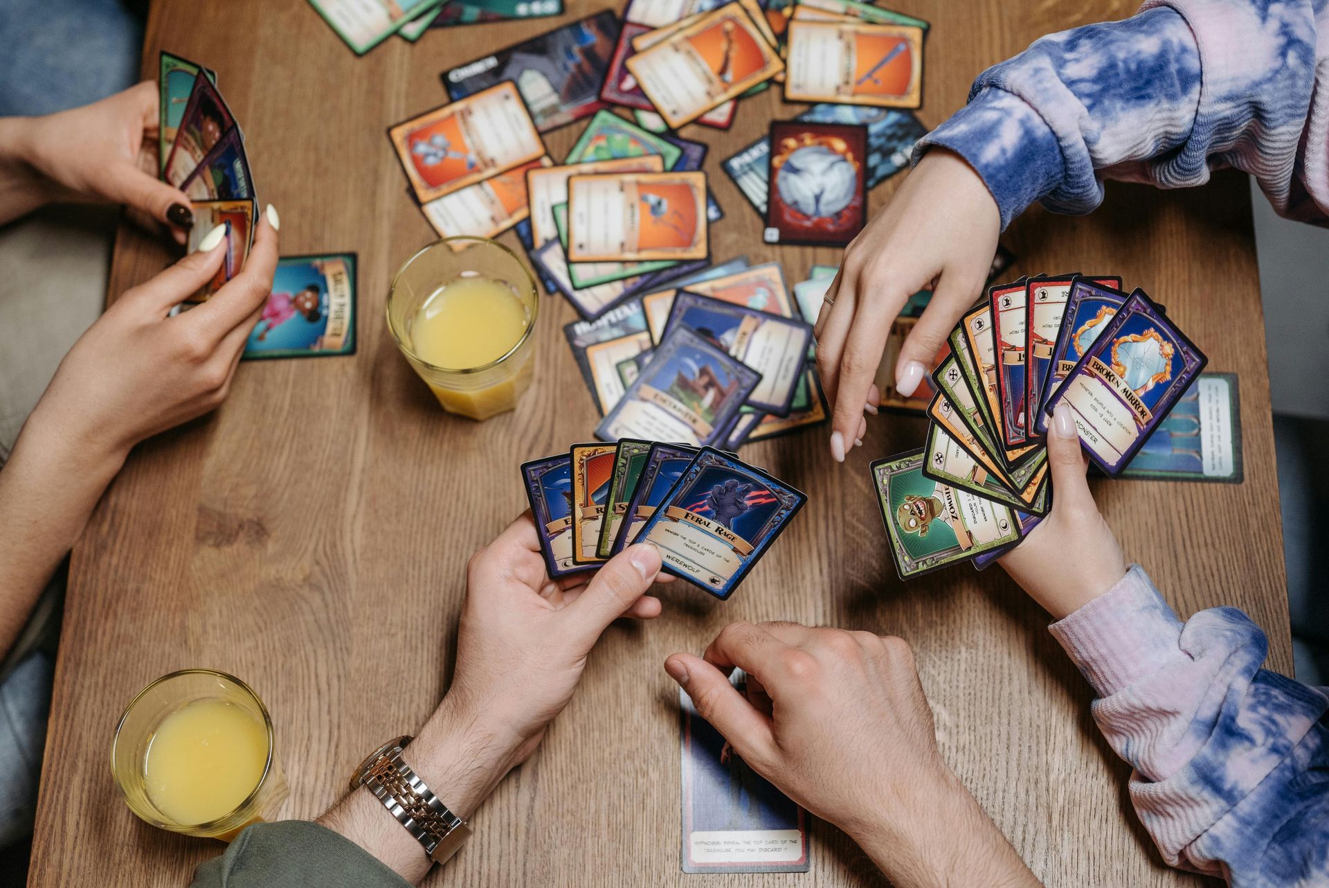 People playing a card game around a wooden table with glasses of juice.