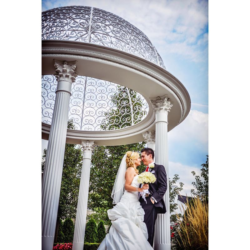 A bride and groom are posing for a picture under a gazebo.