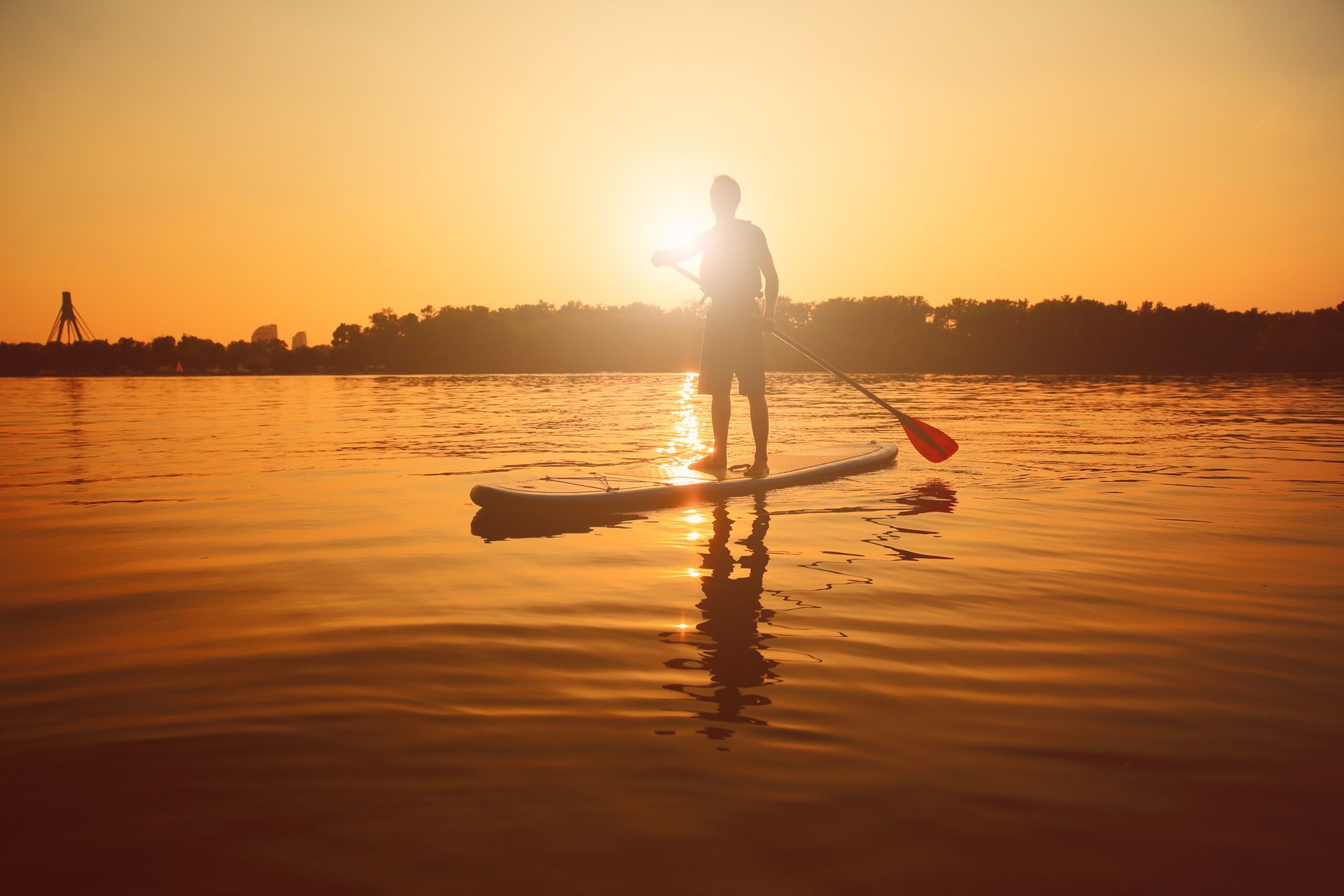 A man is standing on a paddle board in the water at sunset.