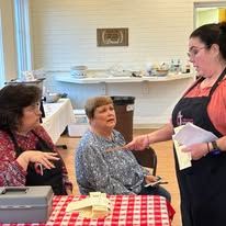 Three women are sitting at a table with a checkered tablecloth talking to each other.