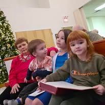 A group of children are sitting in front of a christmas tree.
