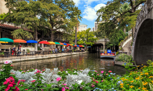 A boat is going down a river surrounded by flowers and umbrellas.