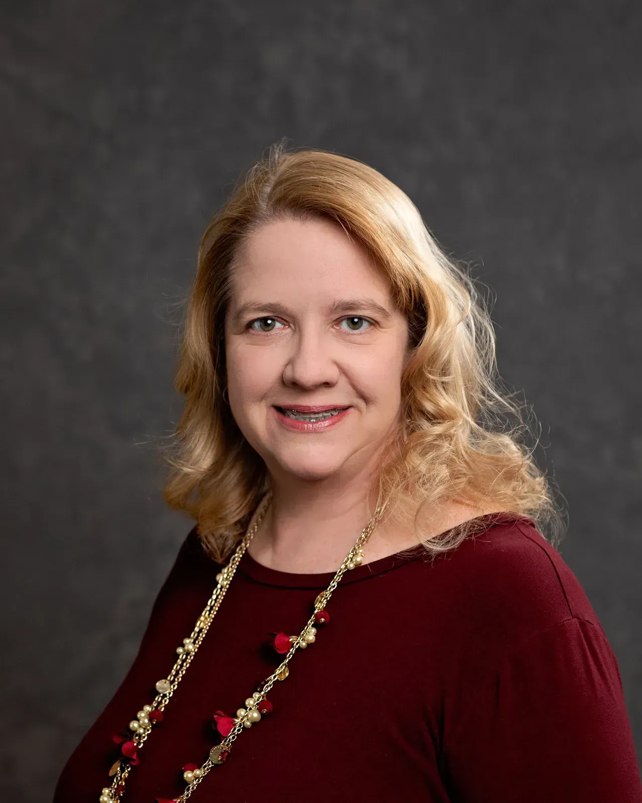 A woman wearing a red sweater and a red necklace is smiling for the camera.