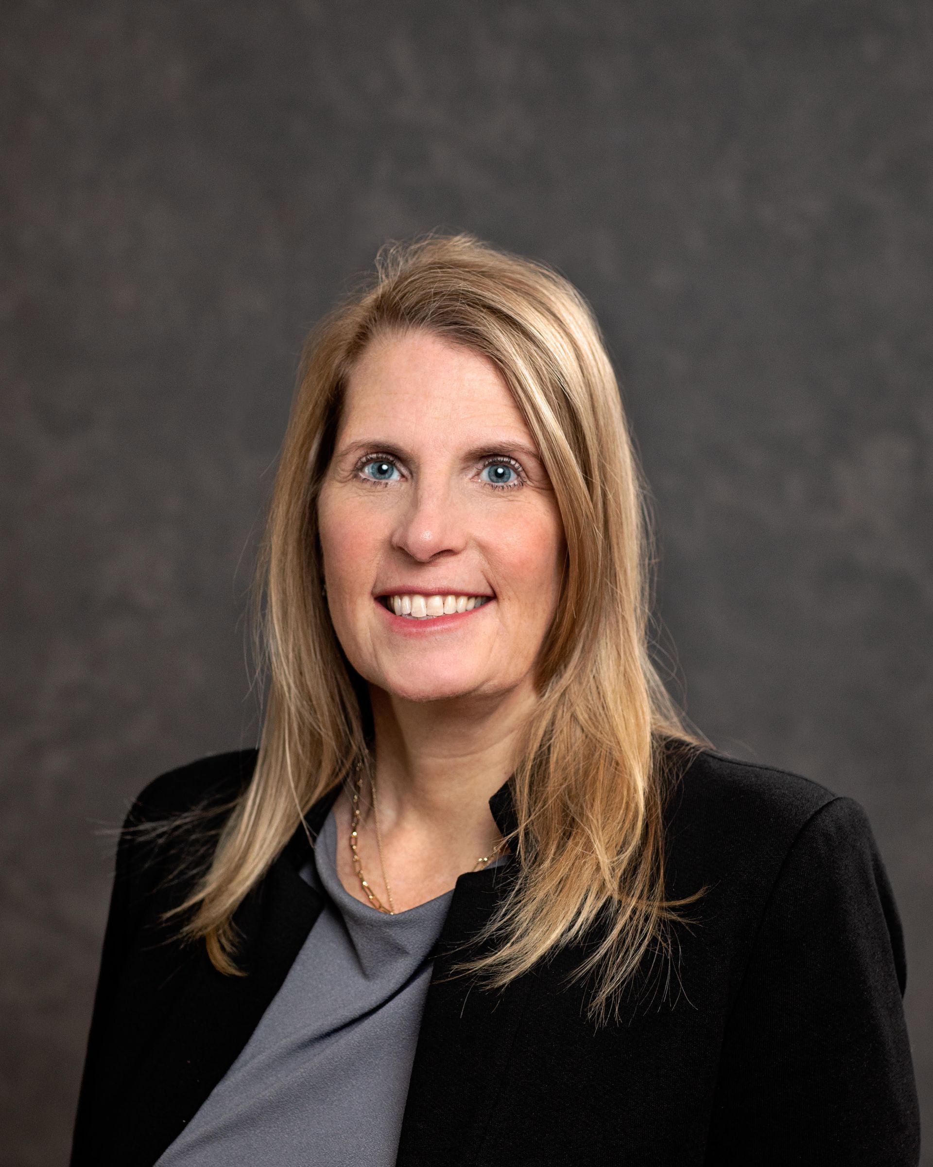 A woman in a black jacket and gray shirt is smiling for the camera.