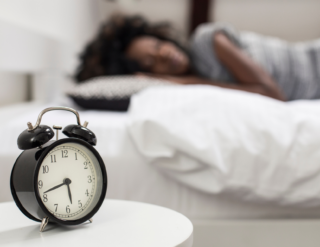 A woman is sleeping in a bed next to an alarm clock.