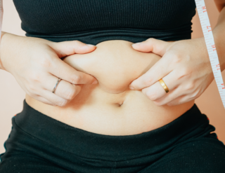 A woman is measuring her stomach with a tape measure