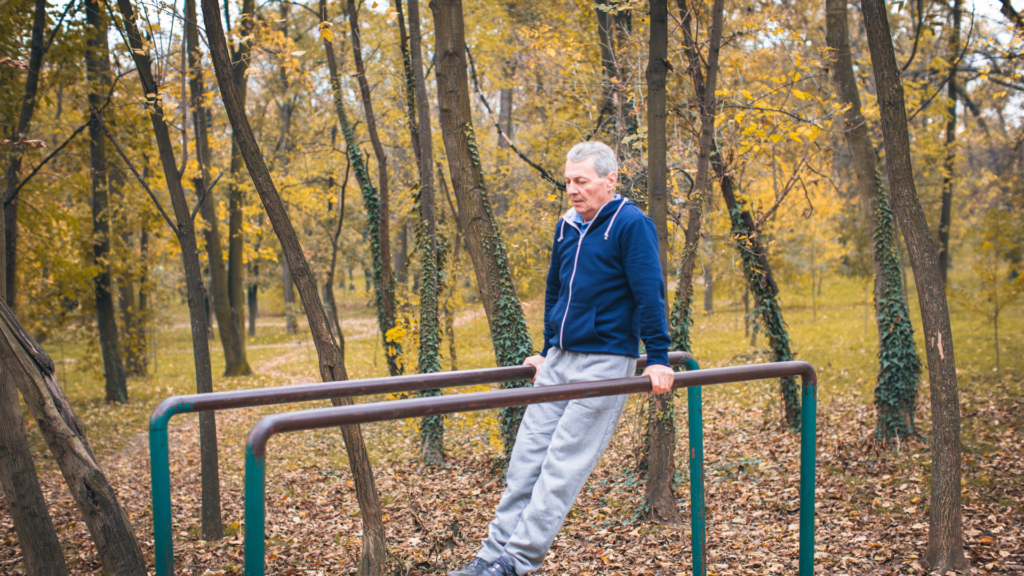 An older man is doing push ups on parallel bars in the woods.