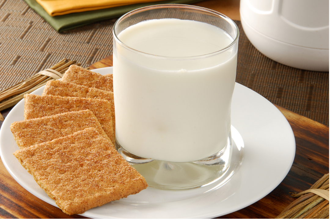 A glass of milk and crackers on a plate on a table.