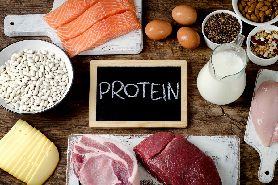 A chalkboard with the word protein written on it is surrounded by different types of protein foods.