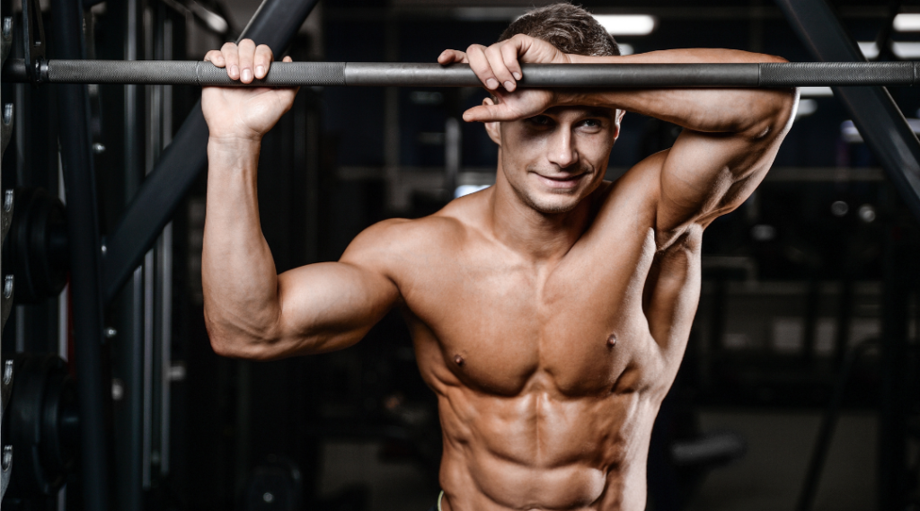 A shirtless man is doing pull ups on a bar in a gym.