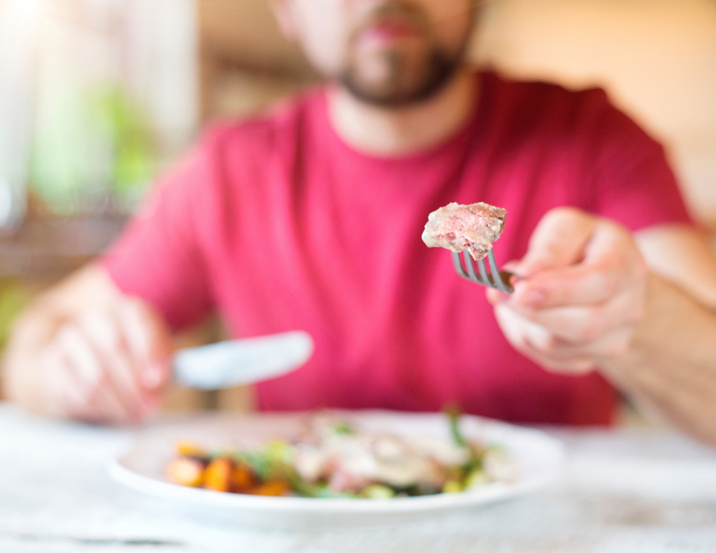 A man is sitting at a table eating a piece of meat with a fork.