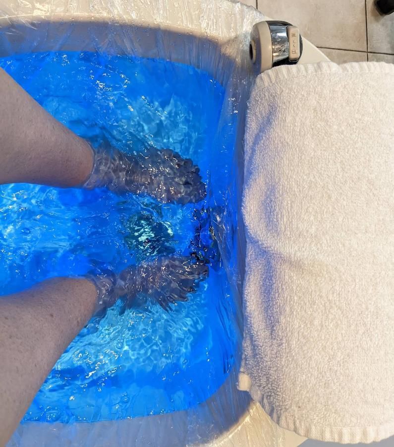 Feet soaking in blue-lit water in a foot spa, next to a white towel.
