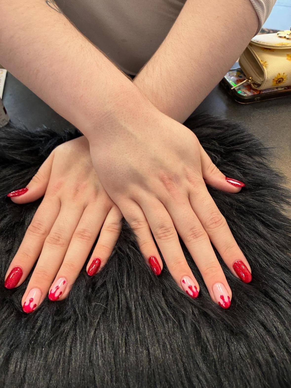 Hands with red and pink nail art on a dark furry surface.