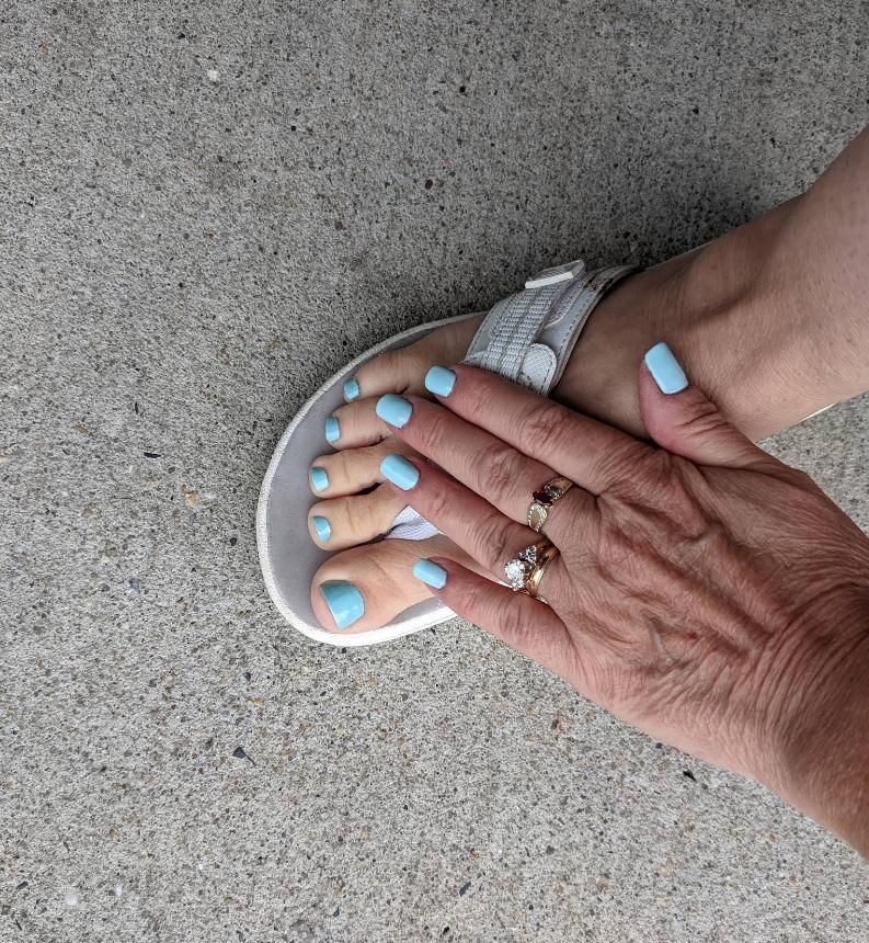Foot in a white sandal with blue toenails.
