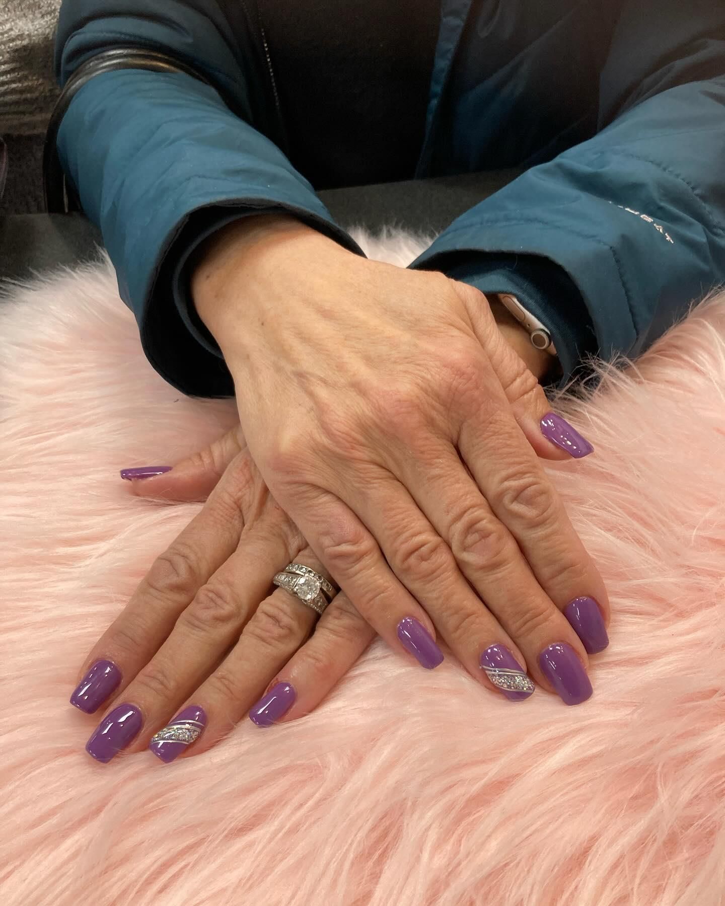 Hands with purple nail polish and a silver accent on a pink fluffy surface.