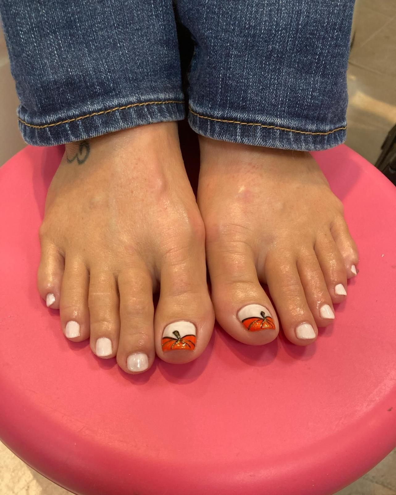 Feet with white toenail polish and pumpkin nail art.