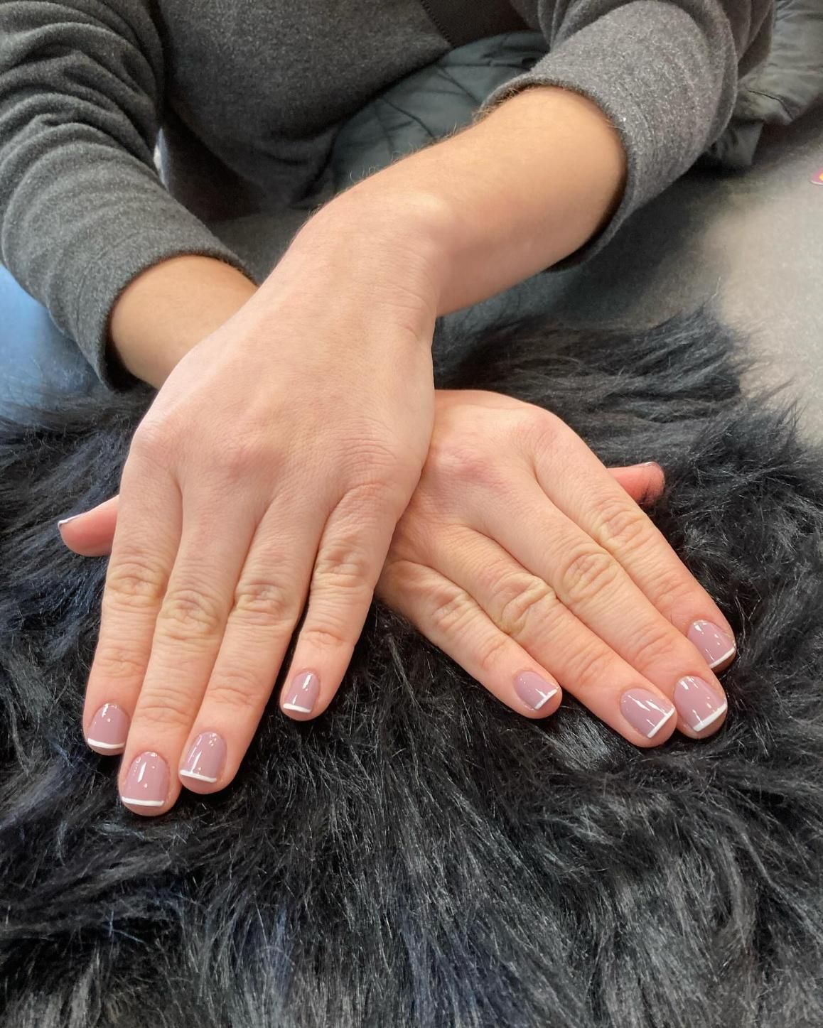 Hands with light pink nails and white tips, resting on black fur.