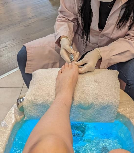 Nail technician using clippers on toenails in salon setting.