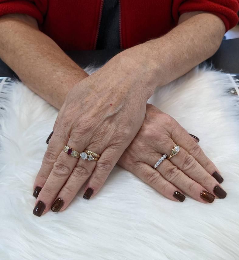 Hands with dark brown nails adorned with rings resting on a white fur.