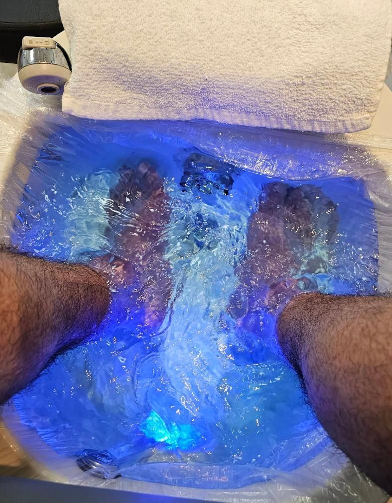 Feet soaking in a foot spa with blue illuminated water.