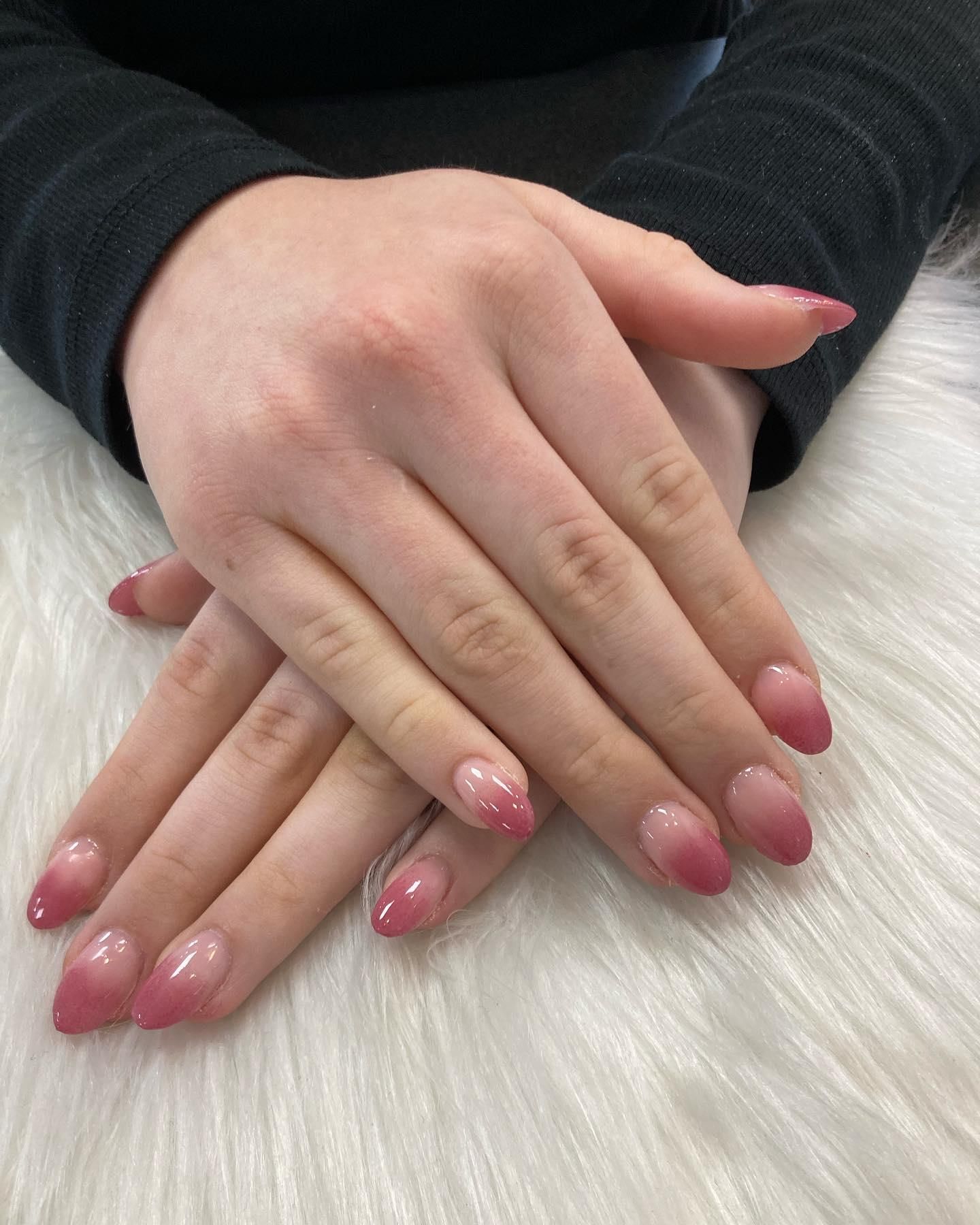 Hands with pink ombre nail polish, crossed on a white furry surface.