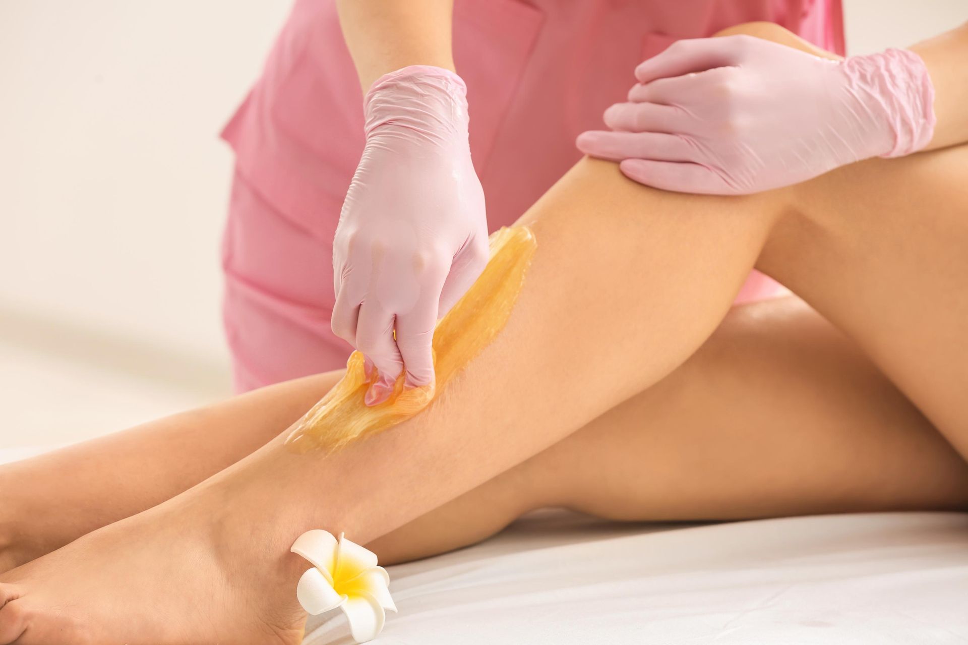 Leg being waxed; esthetician in pink gloves applies wax.