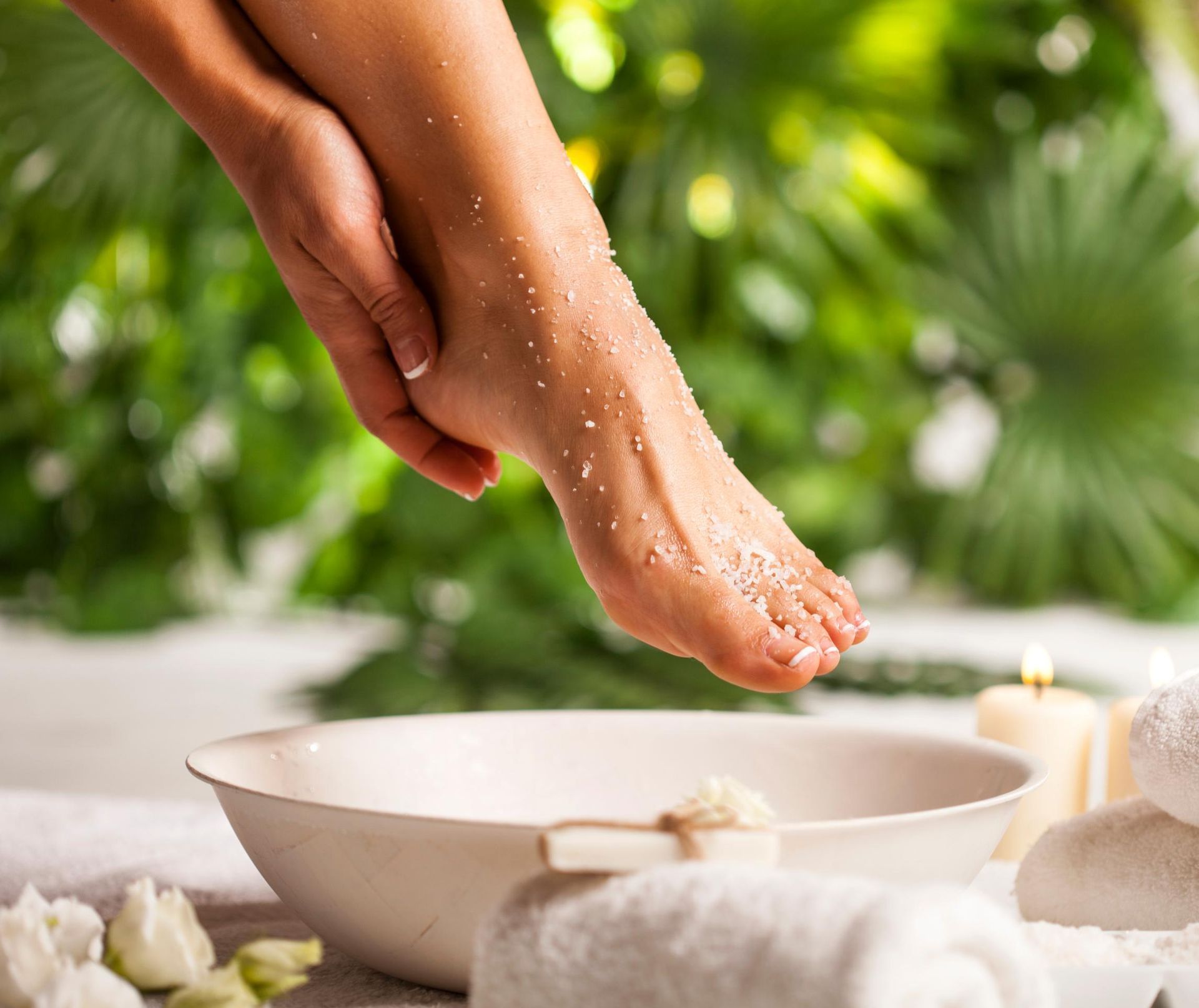 Foot soaking in a bowl with sea salt, hand resting on it.