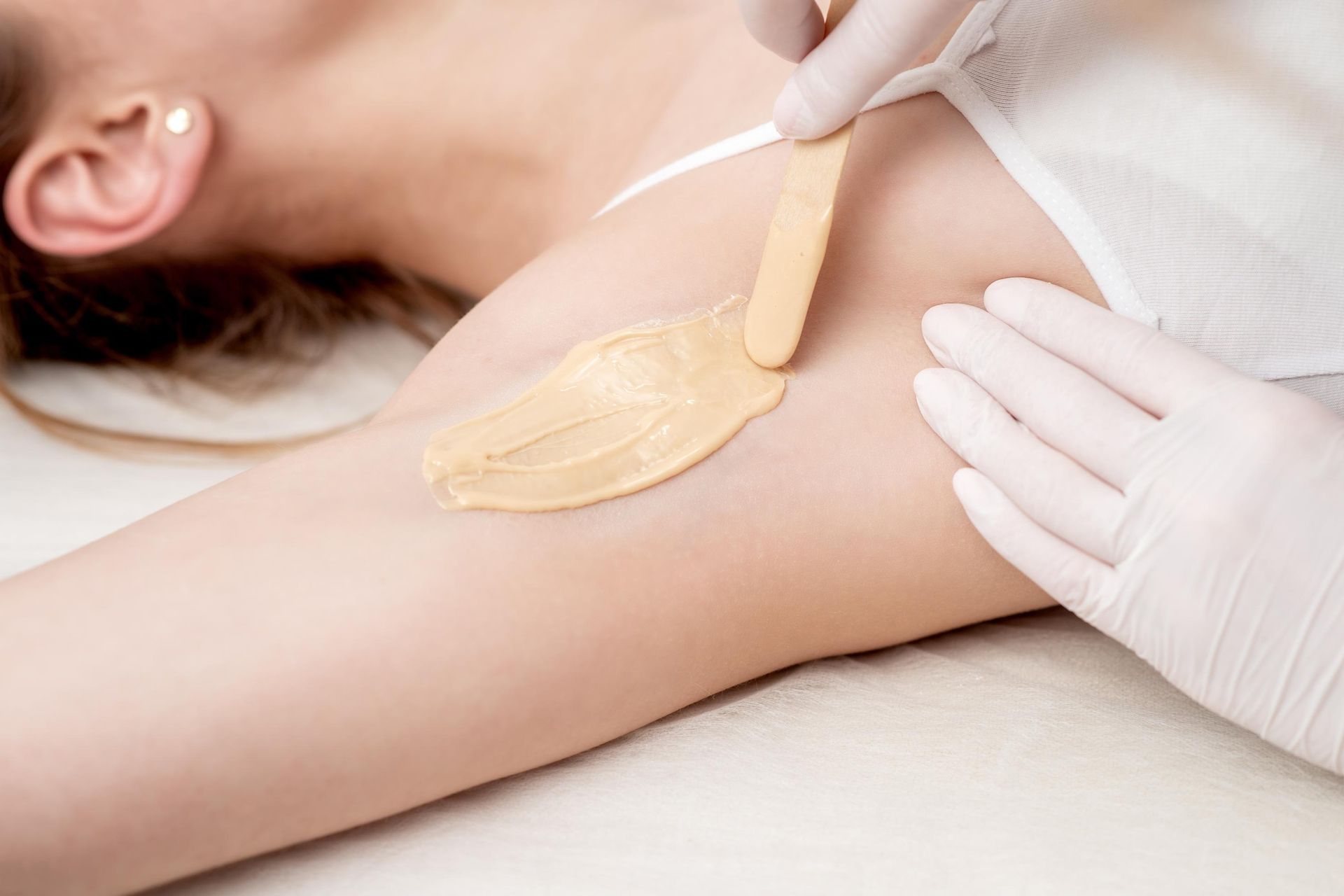 Wax being applied to underarm with a wooden applicator.