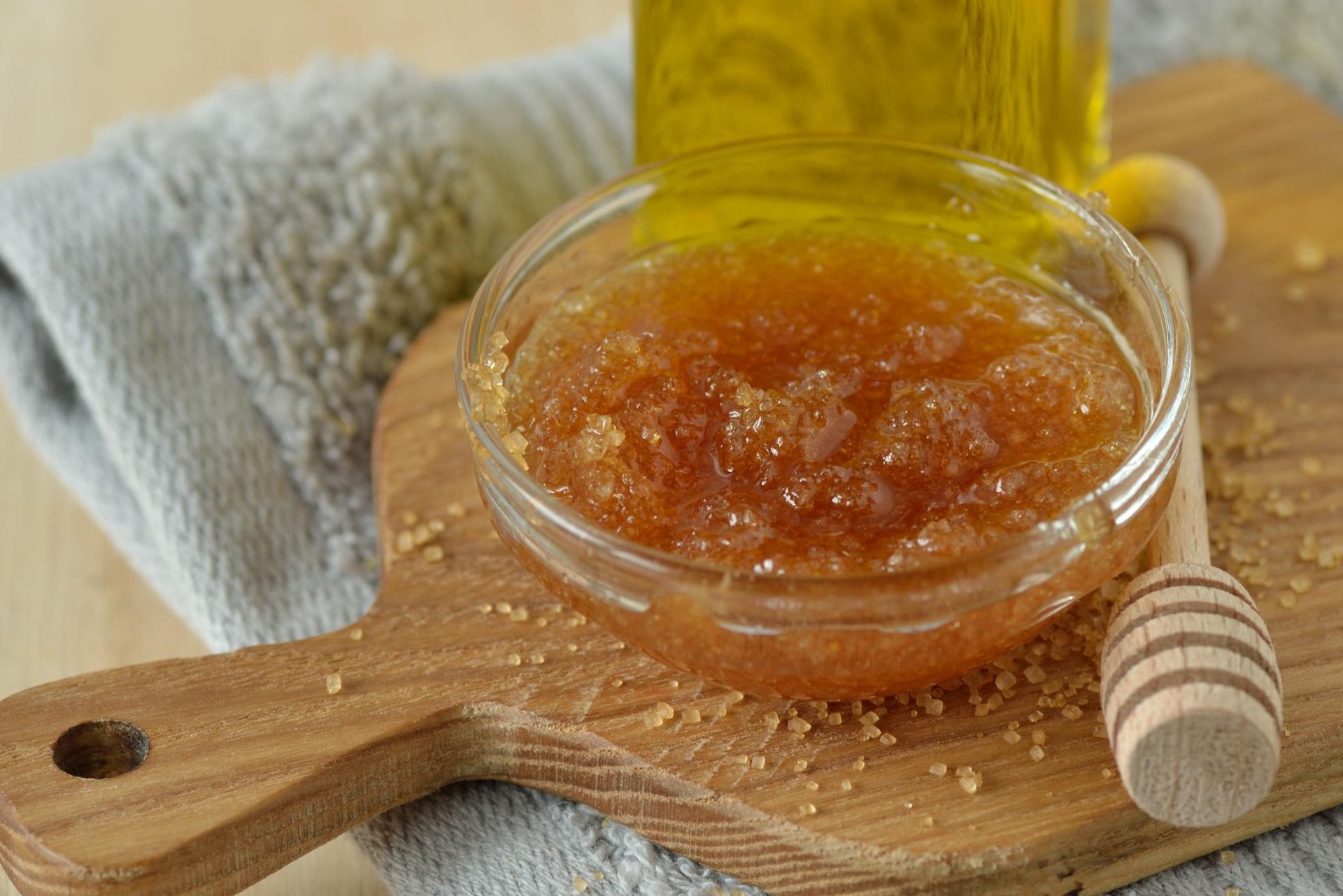 Bowl of brown sugar scrub with honey dipper on a wooden board.