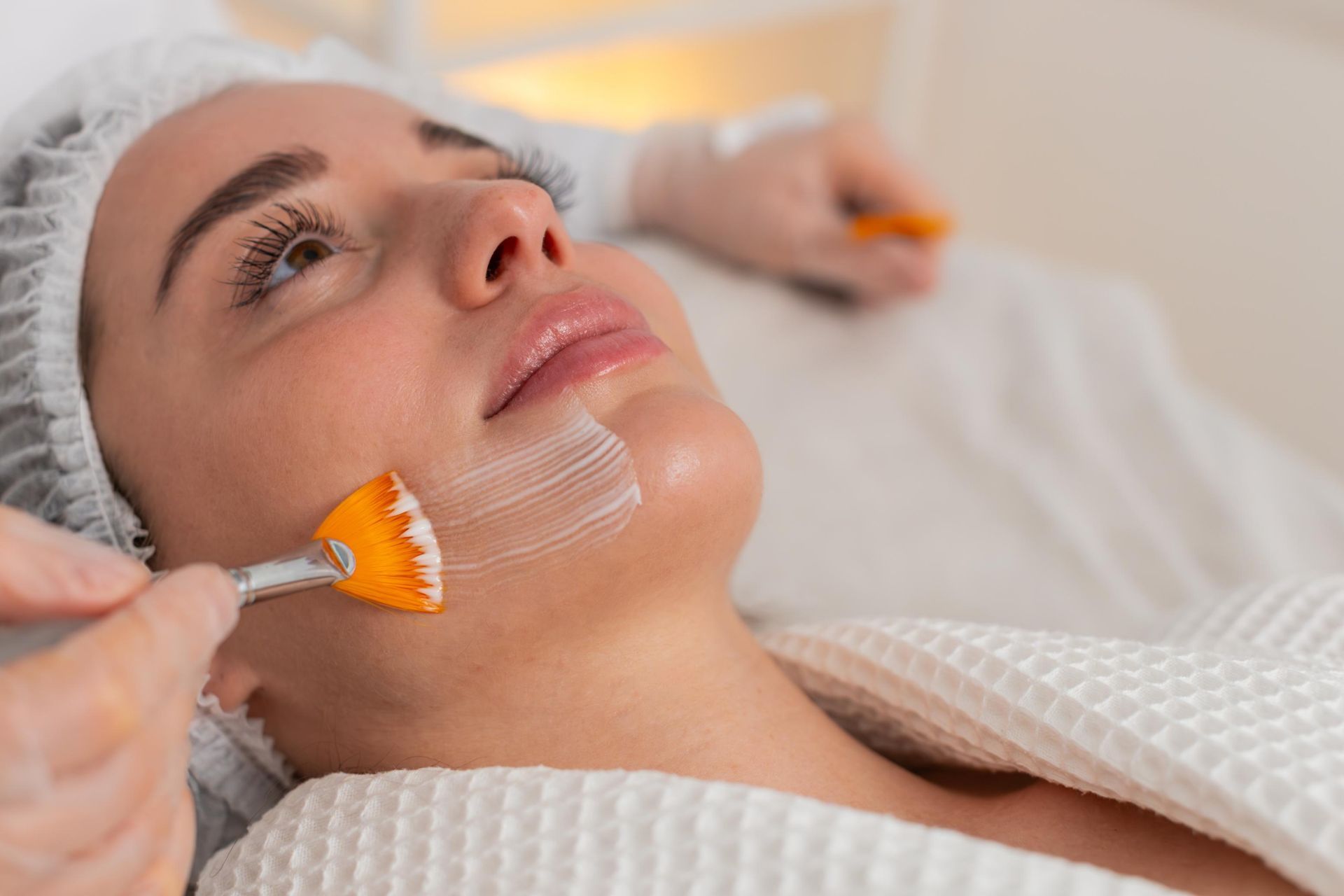 Woman receiving facial treatment, application of a chemical peel, in a salon.