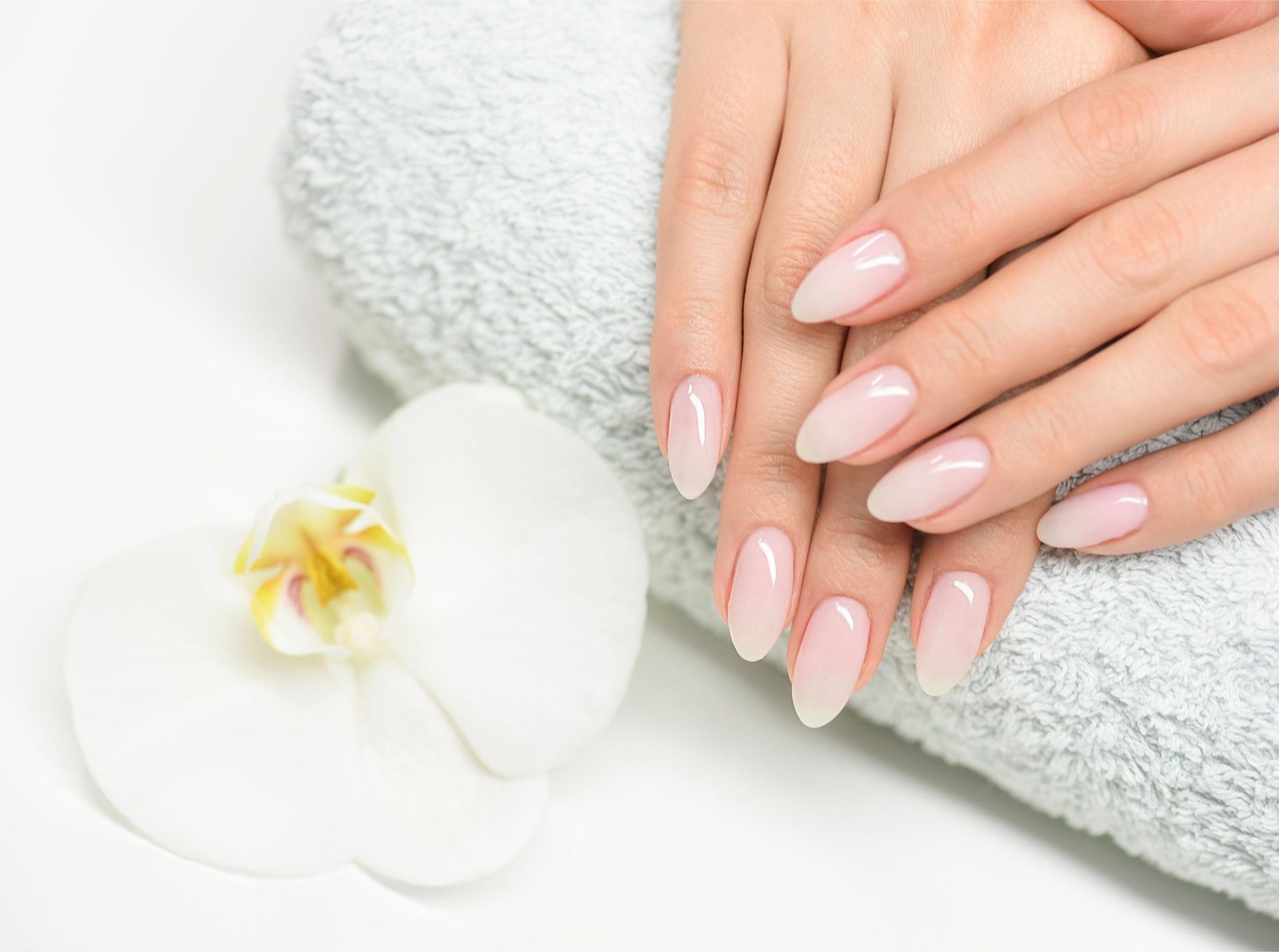 Hands with long, polished nails rest on a folded white towel next to a white orchid flower.