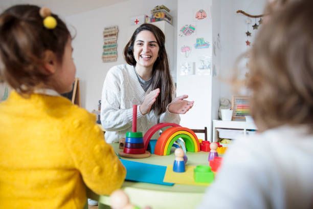 A woman is sitting at a table with children playing with toys.