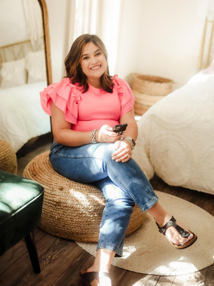 A woman in a pink shirt is sitting on a stool holding a cell phone.