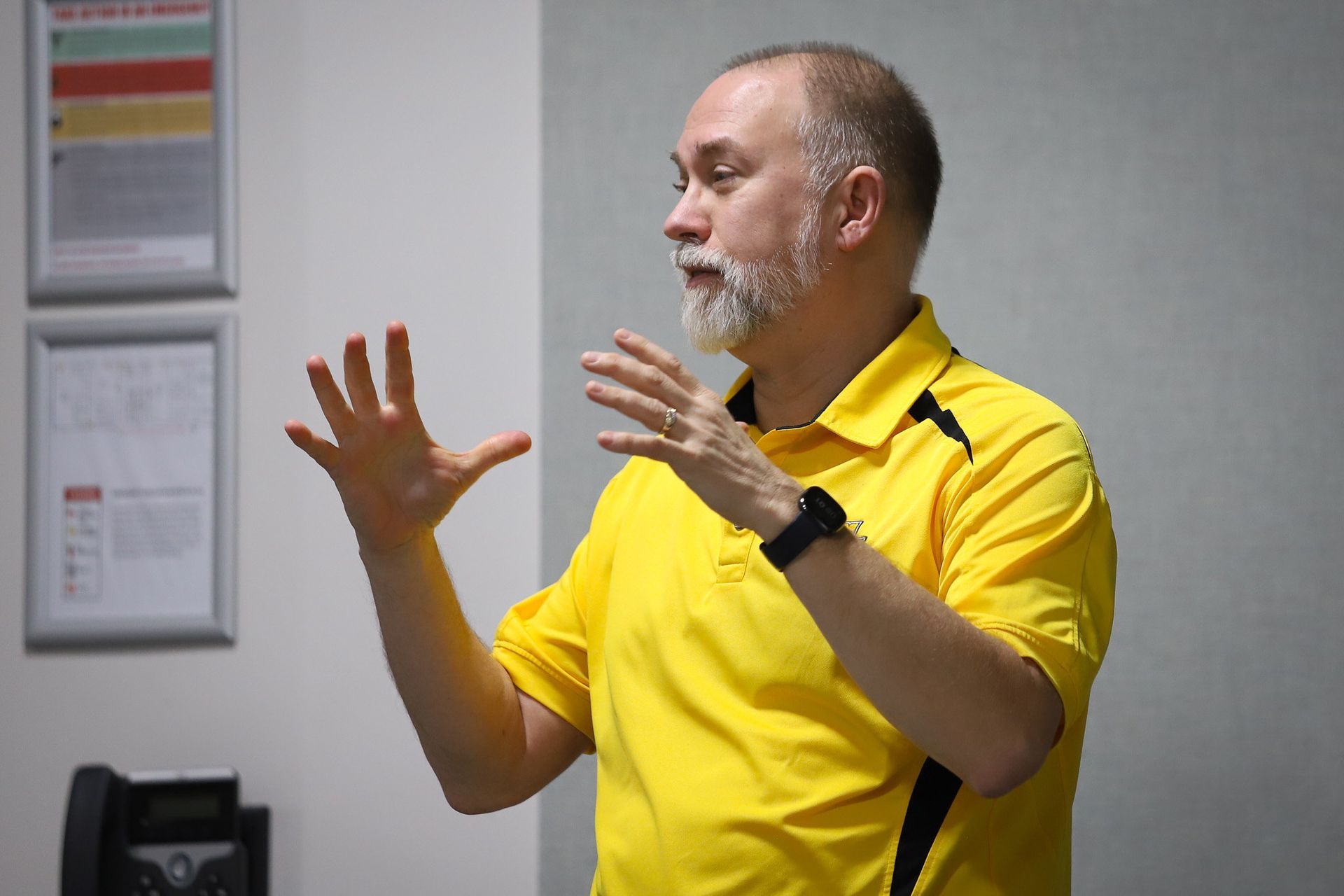 A man in a yellow shirt is talking with his hands outstretched.