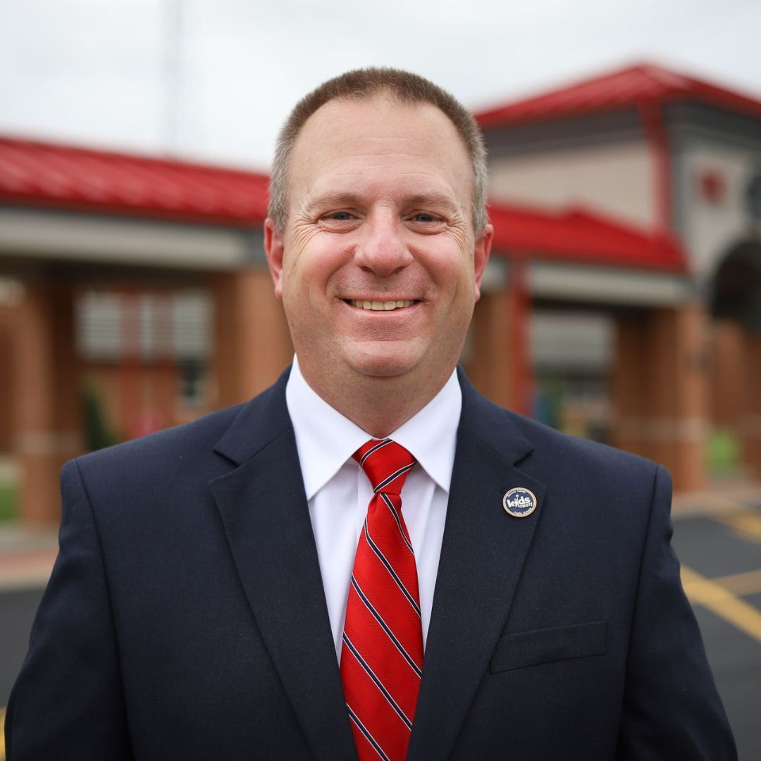 A man in a suit and tie is smiling in front of a building