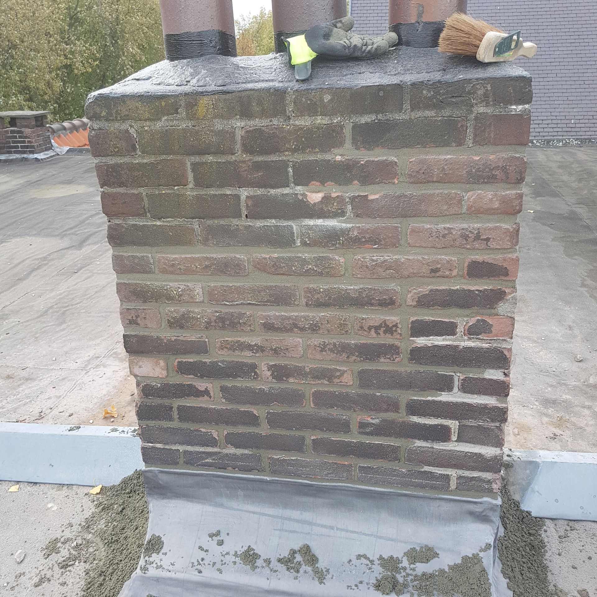 Een bakstenen schoorsteen op een plat dak, afgedekt met keramische rookkanaalvoeringen en gereedschap; bewolkte verlichting.