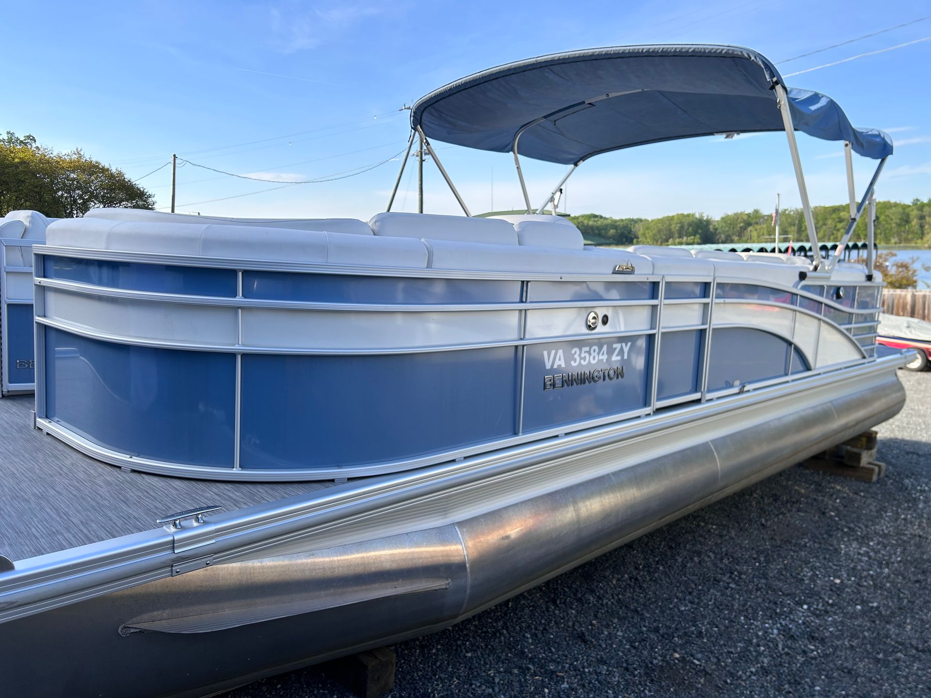 A blue and white Bennington SX Series pontoon boat with a Bimini top is parked on land