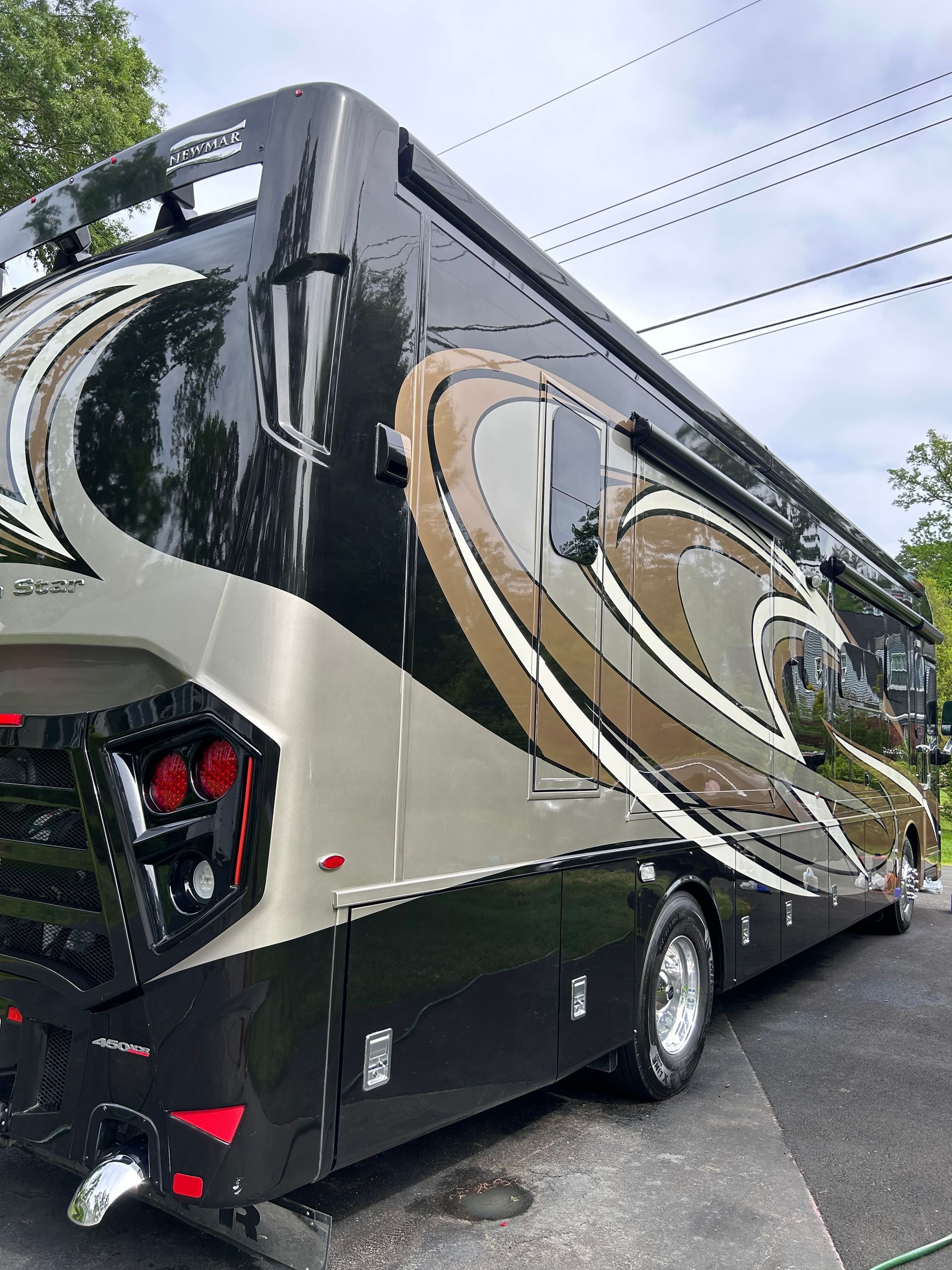 Black and gold Newmar Dutch Star luxury motorhome is parked on a driveway, viewed from the rear side.