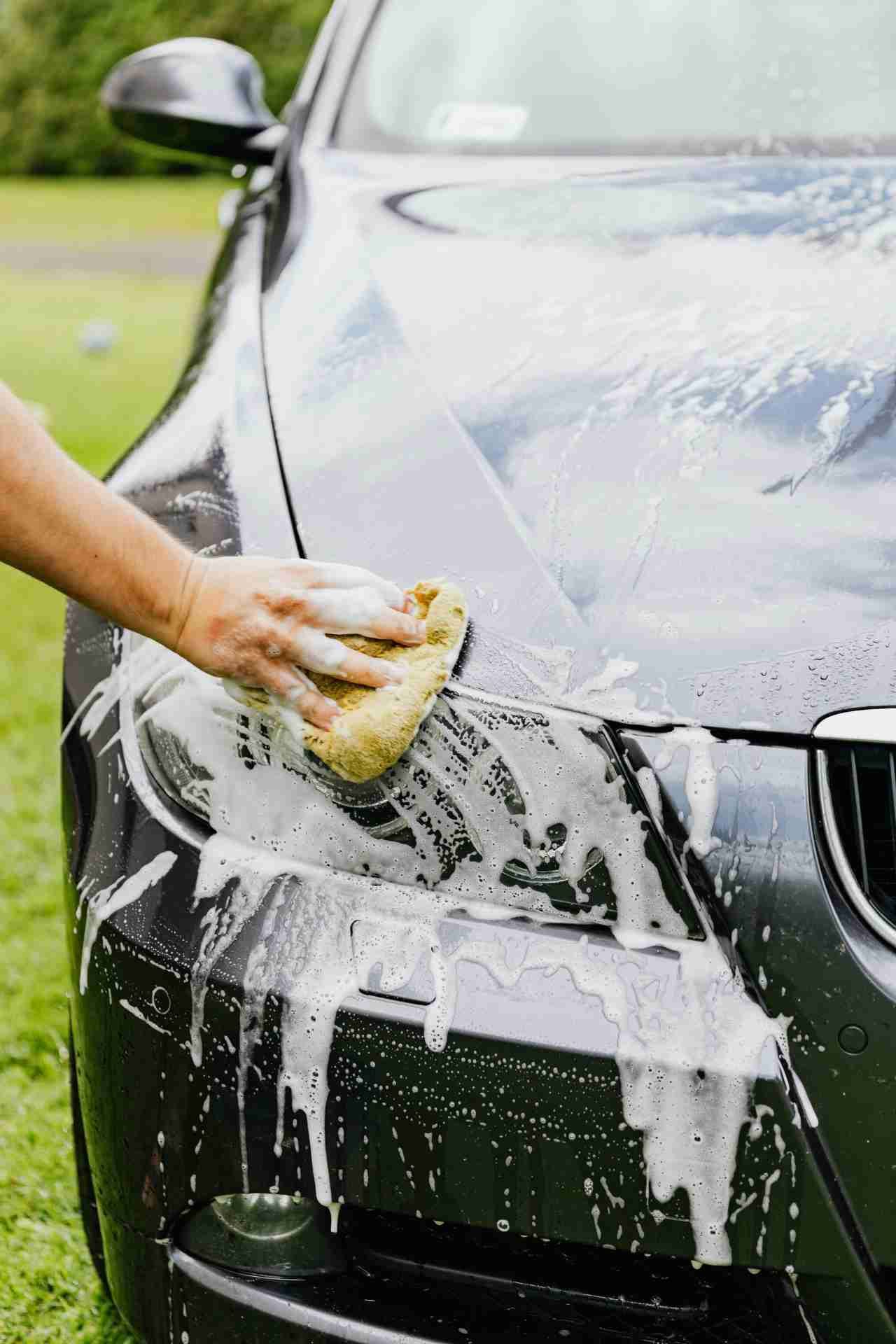Person using a sponge to hand wash car exterior with water and soap.