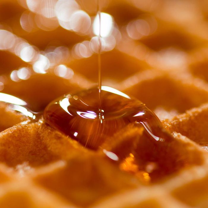 a close up of syrup being poured on a waffle .