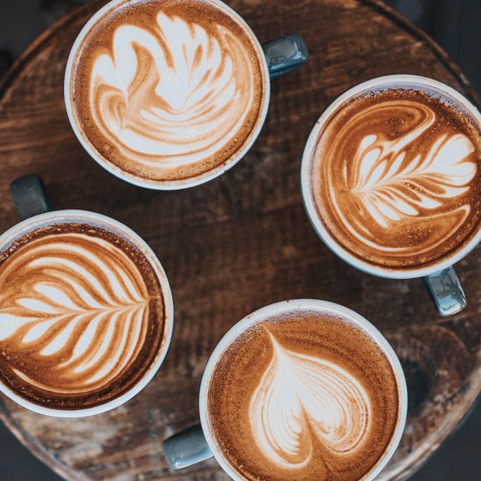 four cups of coffee with latte art on a wooden table