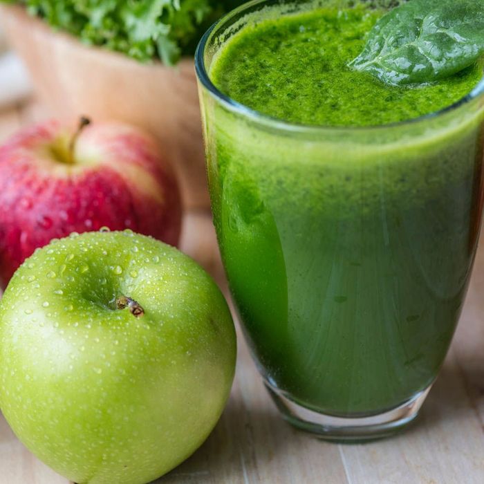 a green smoothie in a glass next to a green apple .