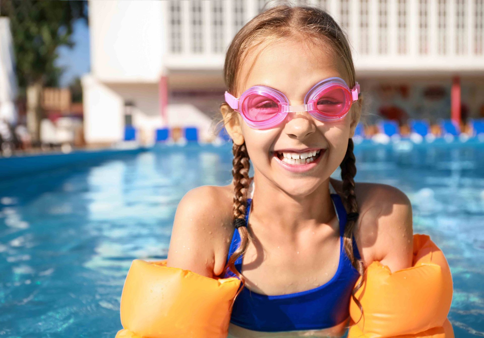 A girl with pool goggles smiling at the edge of a swimming pool