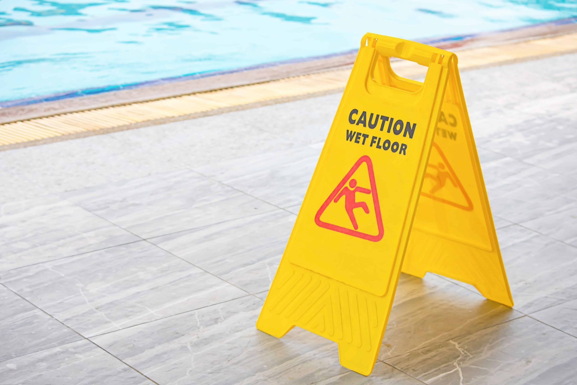 A wet floor sign on a pool deck by a pool