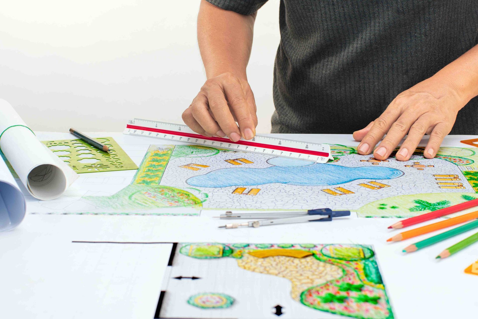 A person with a ruler and pencils designing a pool and landscape