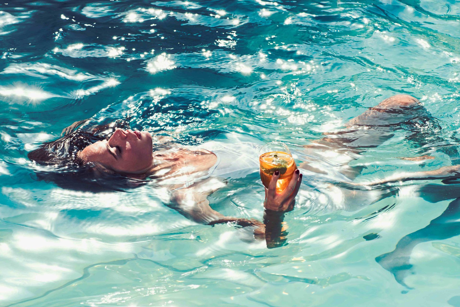 A woman relaxing in the pool water with a drink in her hand