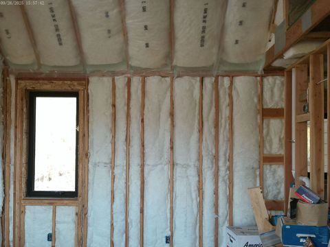Interior view of a room under construction, showing wooden framing, insulation, and a window.