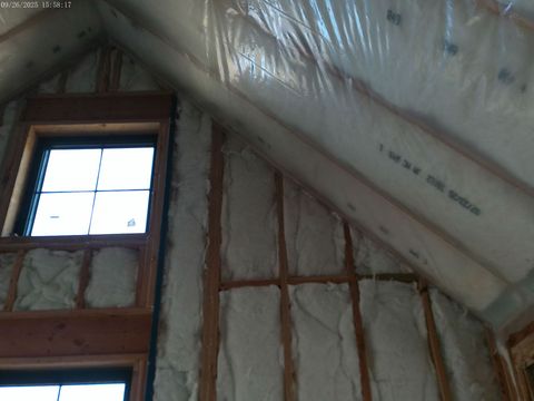 Interior view of a room under construction, with insulation and framing visible around a window and roof.