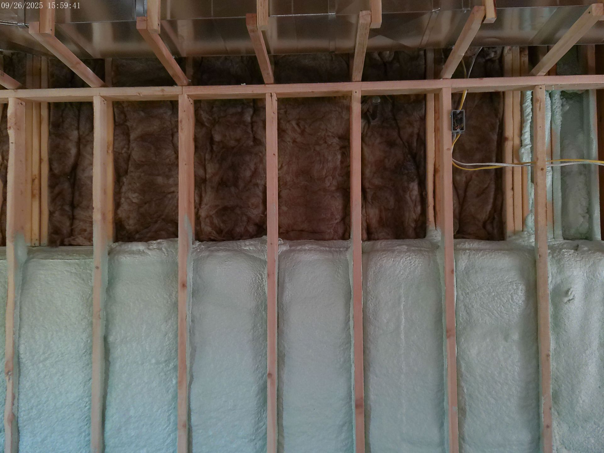 Wall framing with brown insulation above white spray foam, electrical wiring visible.